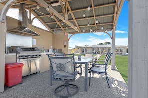 An outdoor patio with a grill, chairs, and a table.