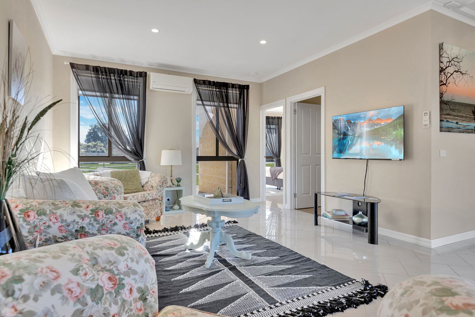 A spacious living room with a sofa, a coffee table, and a flat-screen TV mounted on the wall.