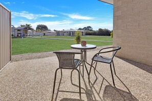 An outdoor patio with two wicker chairs and a round table, a small potted plant, and a view of a residential area with houses and a lawn.