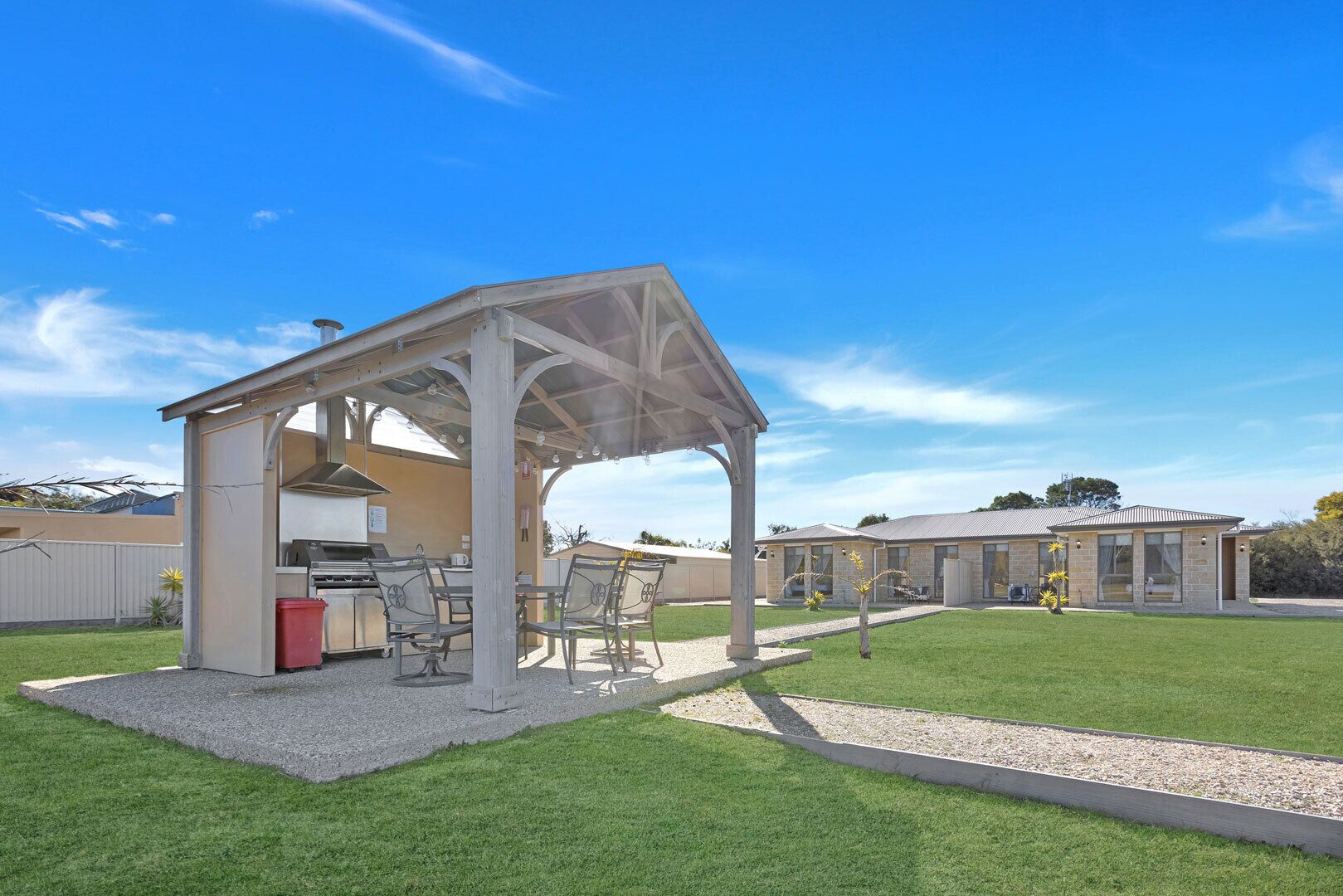 A covered outdoor area with a barbecue setup, seating, and a building in the background.