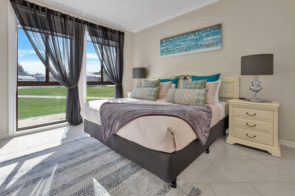 A bedroom with a large bed, a nightstand, a lamp, and a painting on the wall.