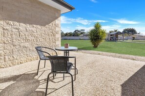 Une terrasse extérieure avec une table et des chaises, une petite table ronde avec une tasse, et un palmier en arrière-plan.