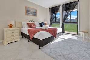 Une chambre à coucher comprenant un lit, des tables de chevet, une commode, une fenêtre avec des rideaux et une vue sur l’extérieur.