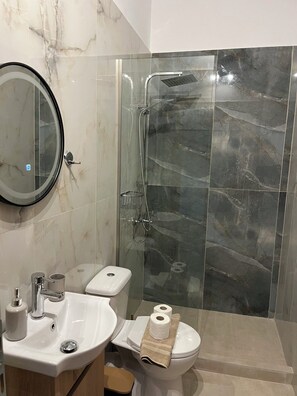Een moderne badkamer met een douchecabine van glas, een wastafel, toilet en een spiegel.