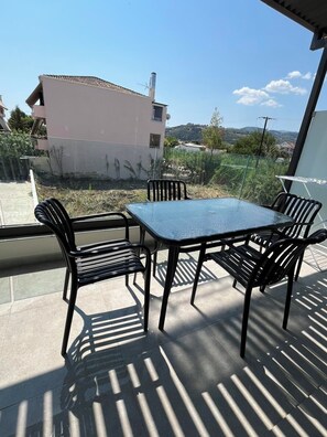 Een terras buiten met een tafel en stoelen, uitzicht op een gebouw en een heldere lucht.