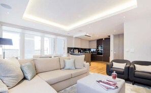 Ein modernes Wohnzimmer mit Sofa, Couchtisch und Essbereich, im Hintergrund eine Küche.