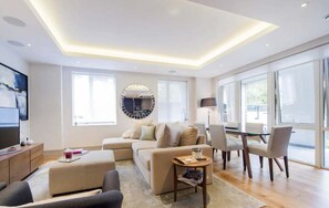 Ein modernes Wohnzimmer mit einer Couch, Sesseln, einem Couchtisch, einem Fernseher und einem Essbereich mit Stühlen und einem Tisch.