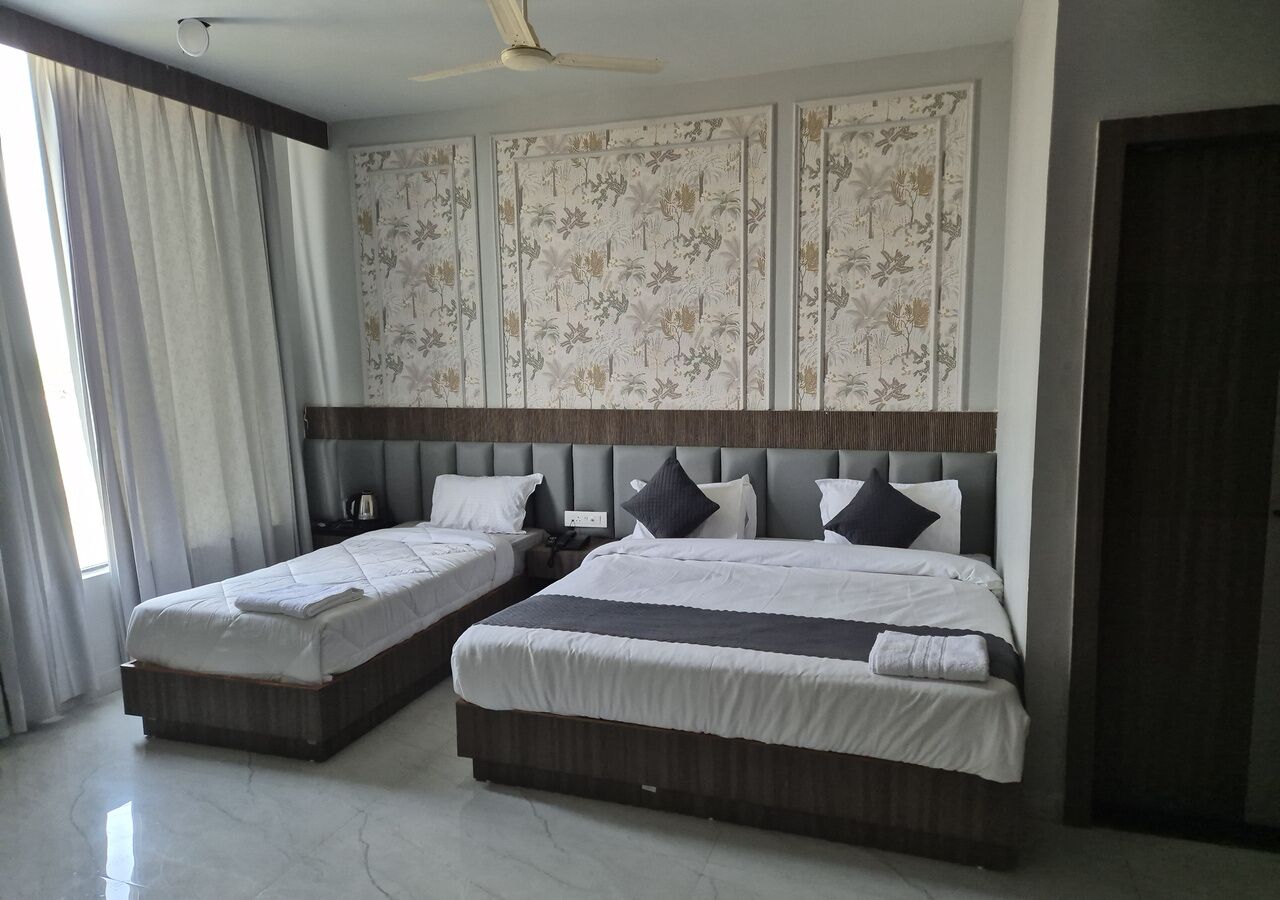A hotel room with two beds, a large window with curtains, a ceiling fan, and a decorative wall panel.