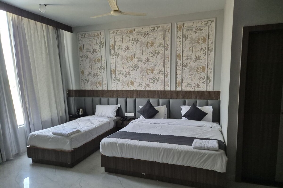 A hotel room with two beds, a large window with curtains, a ceiling fan, and a decorative wall panel.