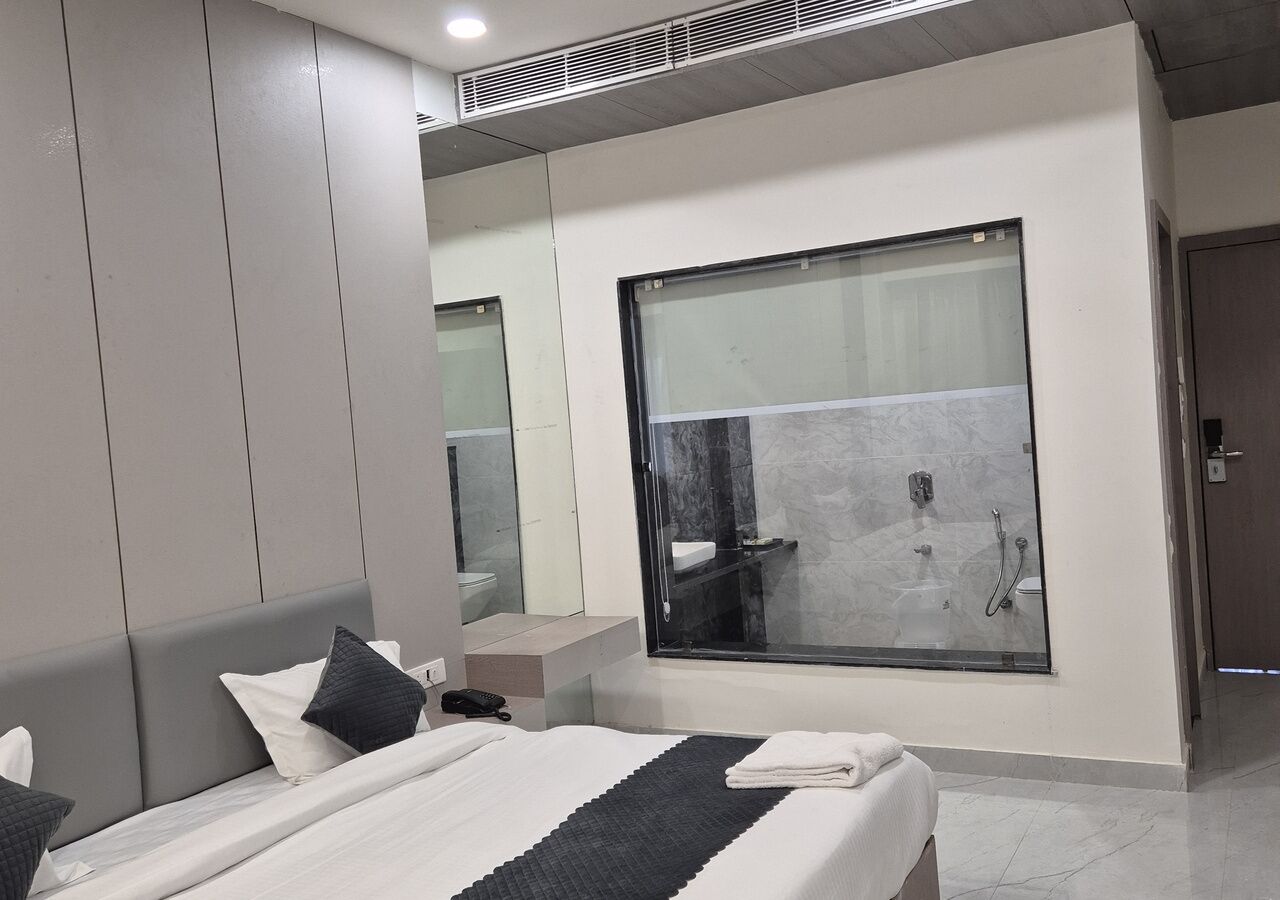 A modern hotel room with a large bed, a bathroom with a glass shower, and a large window.