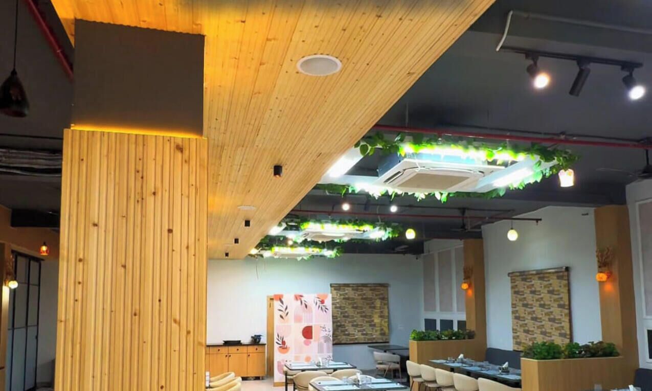 Een restaurantinterieur met houten balken in het plafond, hangende planten en gedekte tafels.