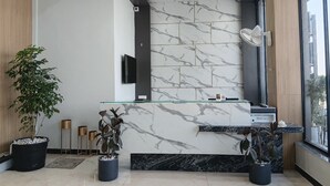 A modern reception area with marble walls, a glass counter, and potted plants.