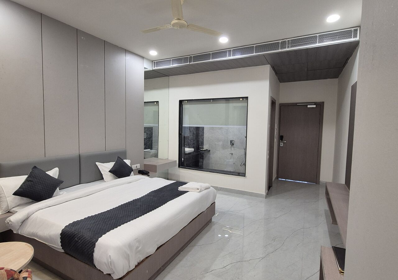 A modern bedroom with a large bed, a bedside table, a mirror, and a shower area.