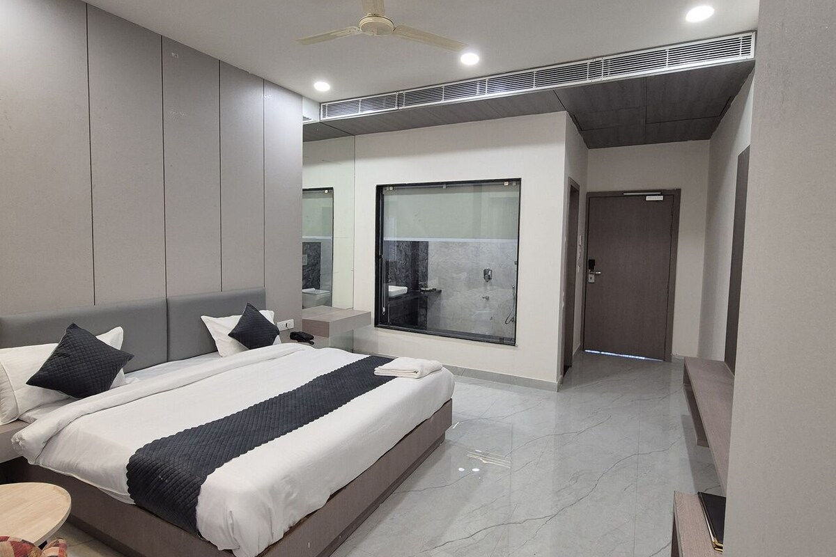 A modern bedroom with a large bed, a bedside table, a mirror, and a shower area.