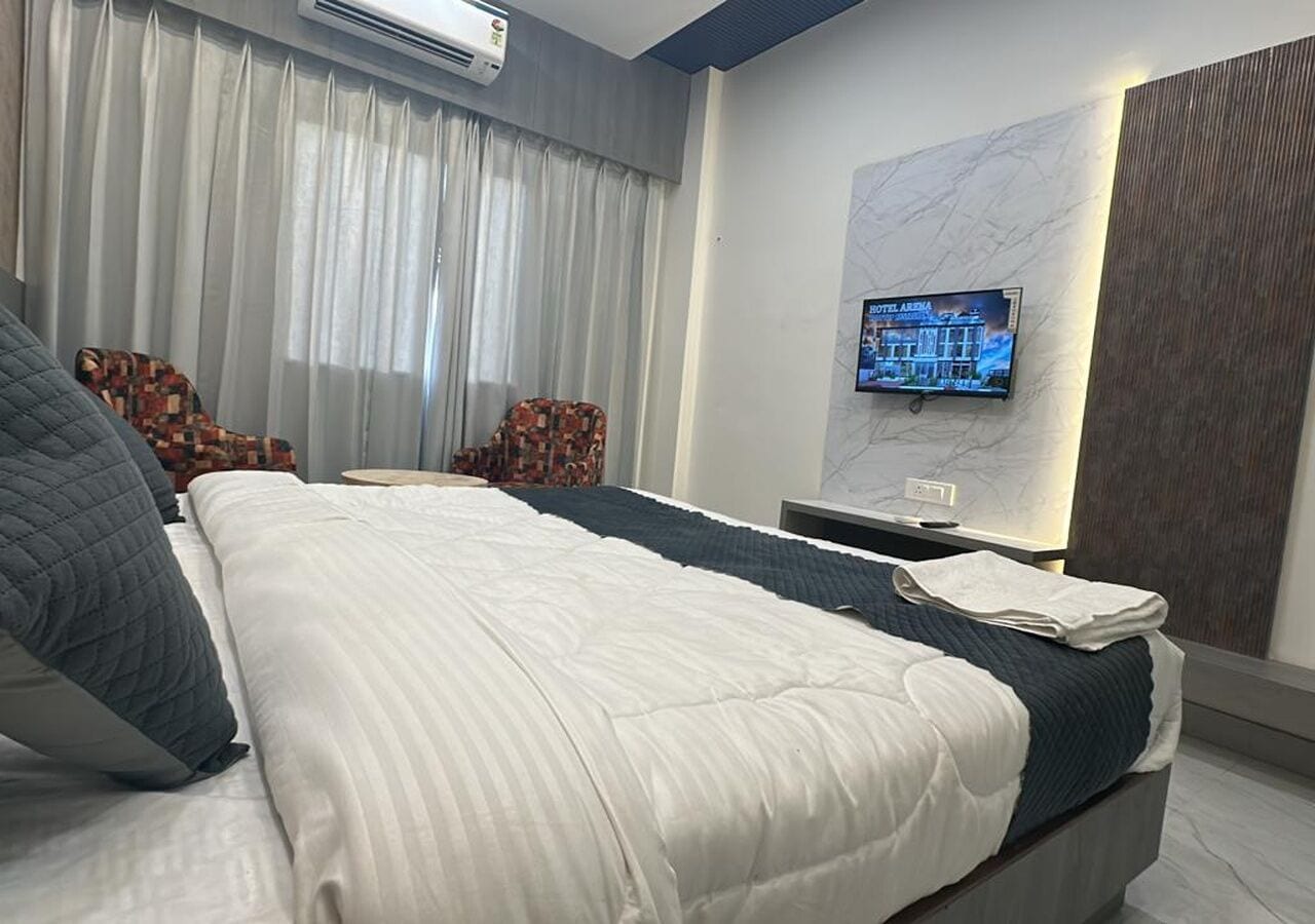 Una habitación de hotel con una cama grande, un televisor en la pared y una ventana con cortinas.