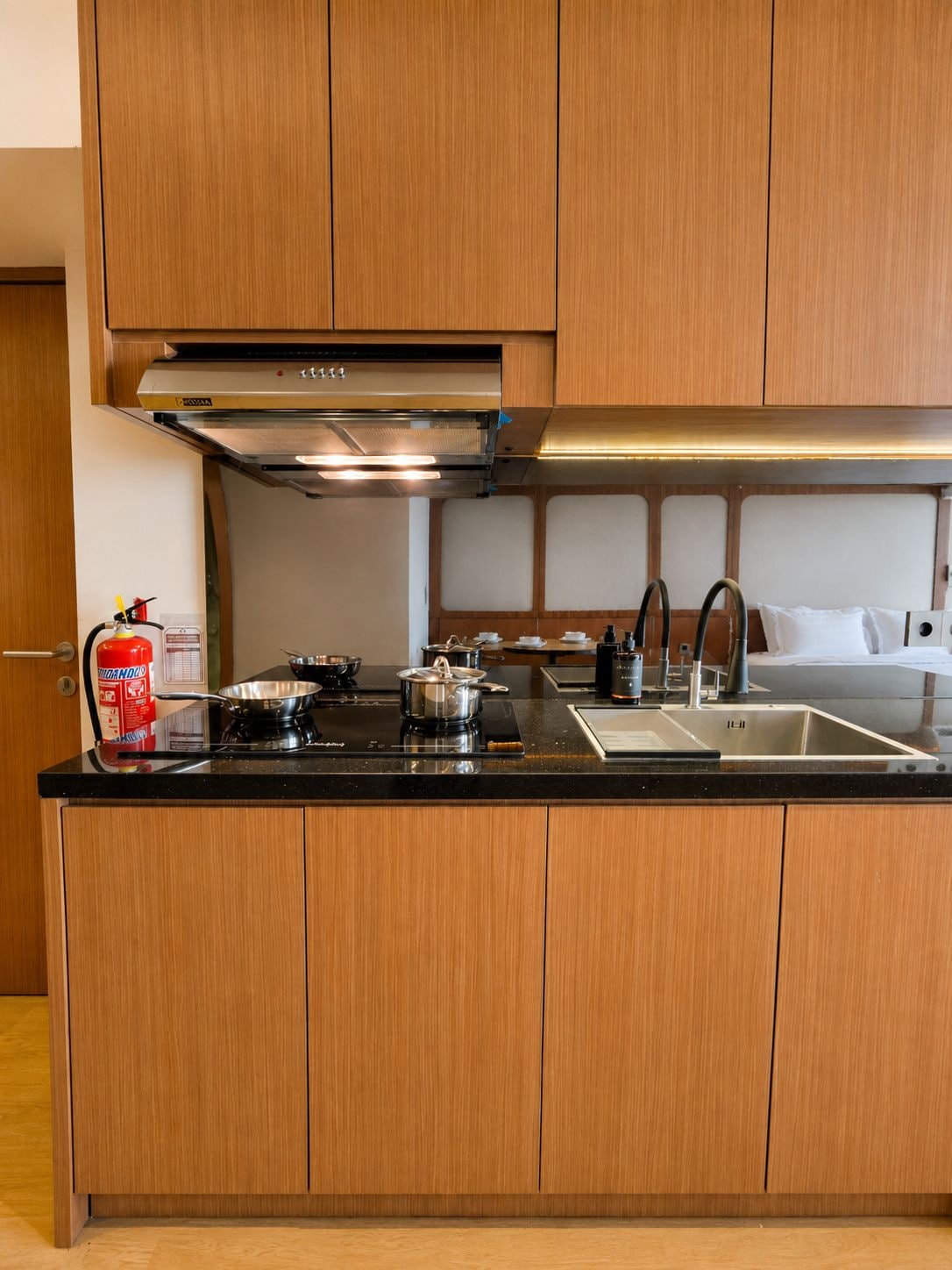 A modern kitchen with wooden cabinets, a stainless steel range hood, a gas stove, a sink, and a fire extinguisher.