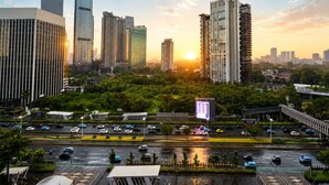 Un paisaje urbano con modernos rascacielos, una autopista concurrida y exuberante vegetación.