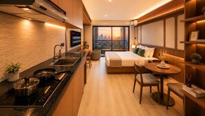 A modern hotel room with a kitchen, a dining area, and a large bed with a city view. - Solana Urban By SanLiving - Senayan (Jakarta)
