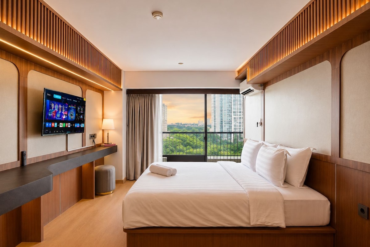 A hotel room with a bed, a TV on a stand, a window with curtains, and a view of the cityscape.