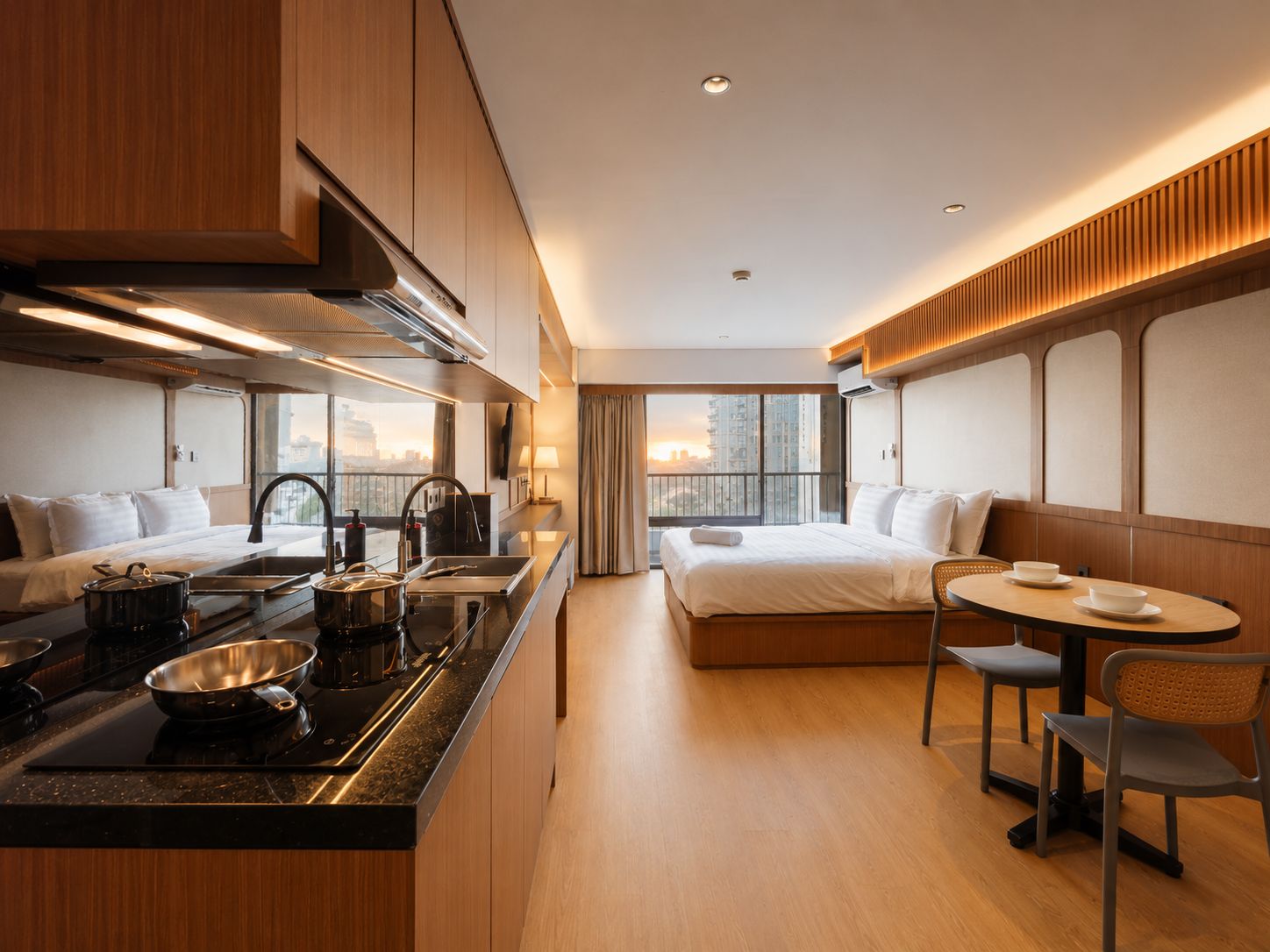 Quarto de hotel moderno com cozinha compacta, cama, área de refeições e grande janela vista para a cidade.