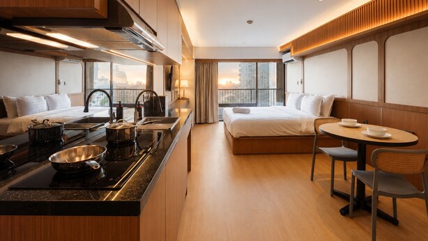 A modern hotel room with a kitchenette, a bed, a dining area, and a large window with a city view. - Solana Urban By SanLiving - Senayan (Jakarta)