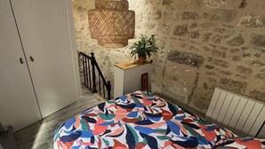 A bedroom with a patterned bedspread, a hanging light fixture, a potted plant, and a stone wall. - Charming house in the city center (Angoulême)