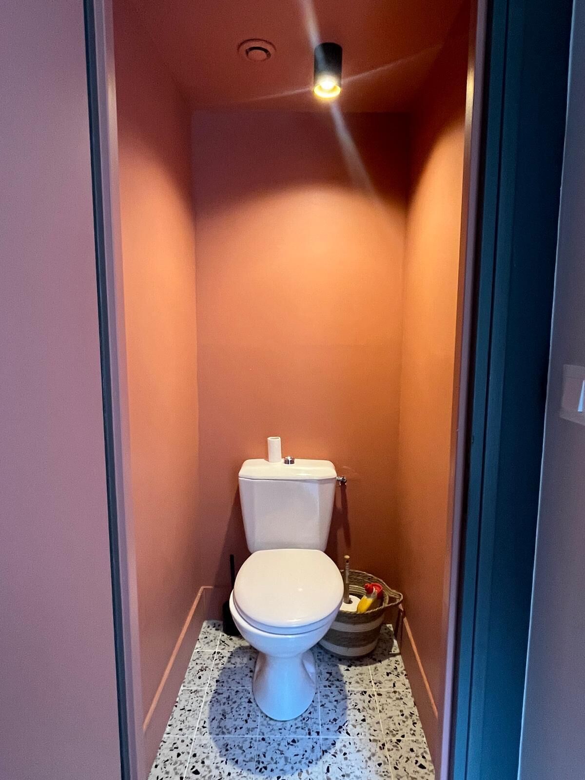 Un bagno piccolo e stretto con il water bianco, pavimento piastrellato e una luce a soffitto.