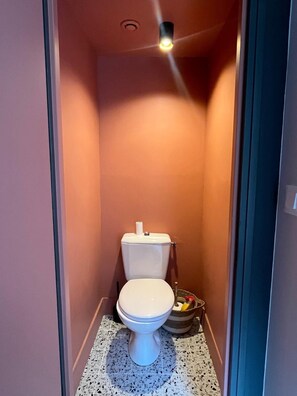 Een kleine, smalle badkamer met een wit toilet, een betegelde vloer en een plafondlamp.