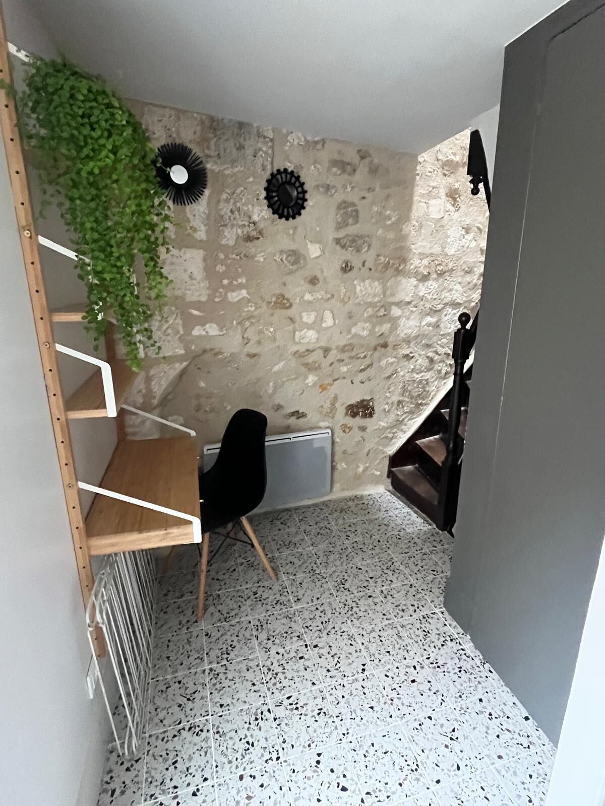 Une pièce de taille modeste avec un mur en pierre, une chaise noire, une étagère en bois et un radiateur.