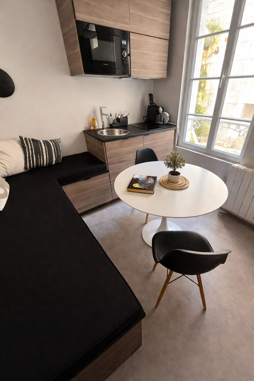 Ein modernes Zimmer mit einem Bett, einem Esstisch mit Stühlen, einer kleinen Küchenzeile und einem Fenster mit Blick.