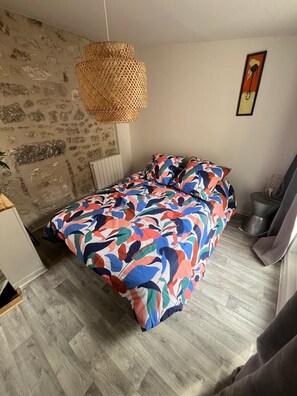 Een slaapkamer met een bed, een hanglamp, een radiator en een schilderij aan de muur.