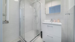 A modern bathroom with a glass-enclosed shower, white tiled walls, and a white vanity with a mirror above. - Apartment Krochmalna 61 (Warszawa)