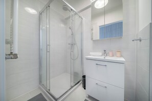 A modern bathroom with a glass-enclosed shower, white tiled walls, and a white vanity with a mirror above. - Apartment Krochmalna 61 (Warszawa)