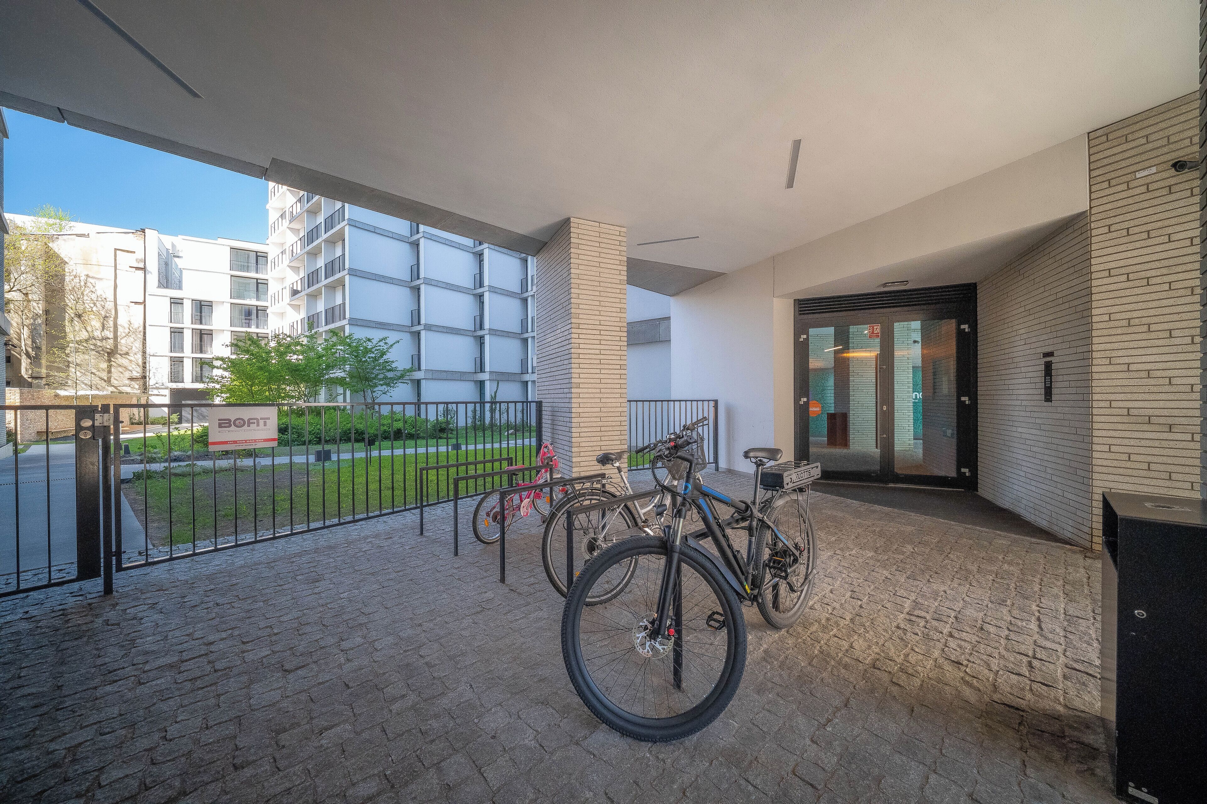 Un espacio al aire libre cubierto con un aparcamiento para bicicletas, un letrero que dice 'BOAT' y la entrada de un edificio con puertas de vidrio.