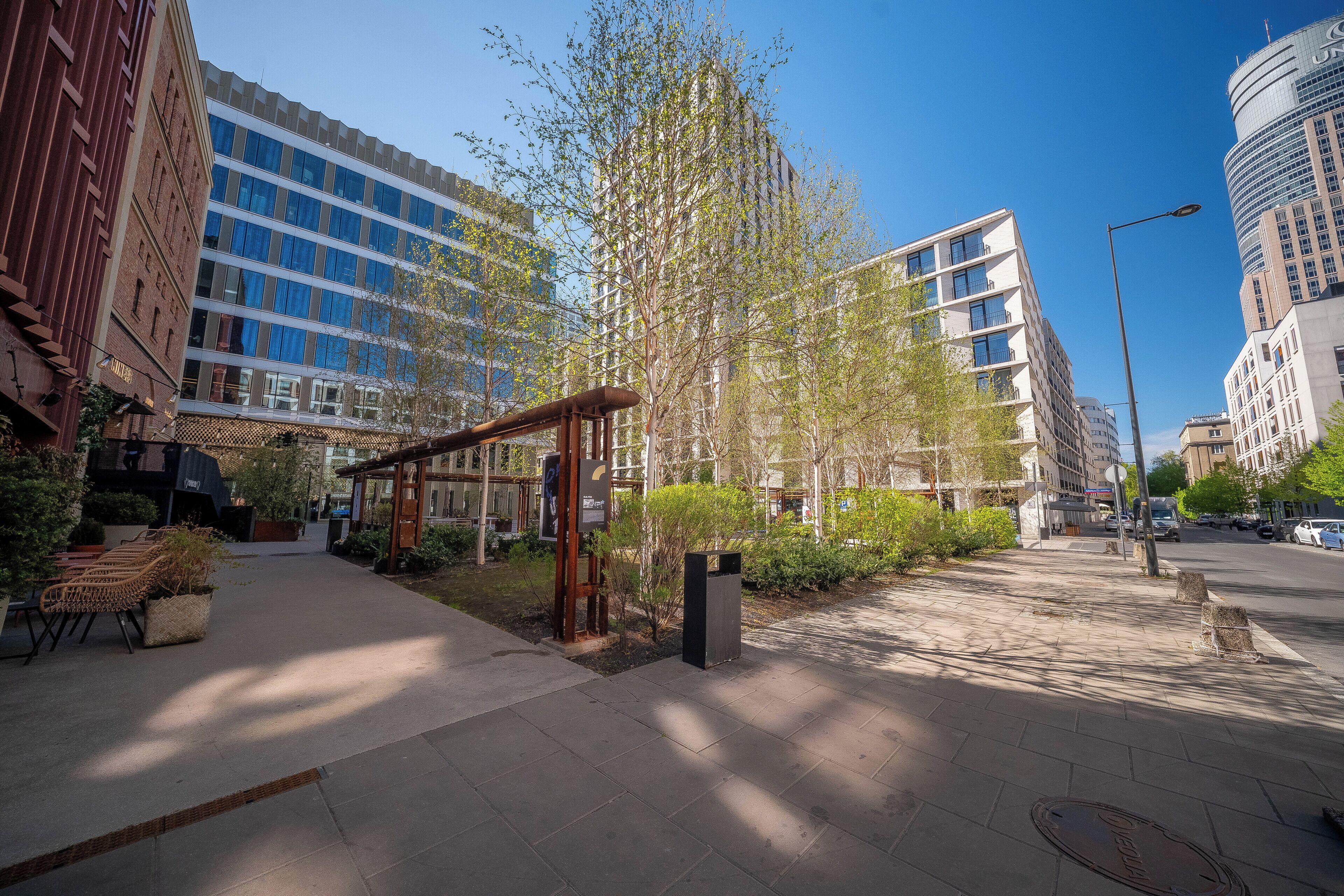 A modern urban street with buildings, a pedestrian walkway, and greenery.