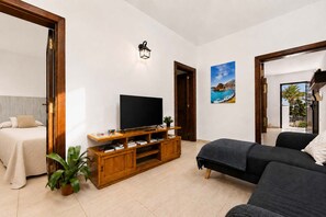 A modern living room with a flat-screen TV, wooden entertainment unit, a sofa, a bed, and a potted plant. - Casa Valeria Lanzarote Terraza BBQ y Jard n Volc Nico (Tinajo)