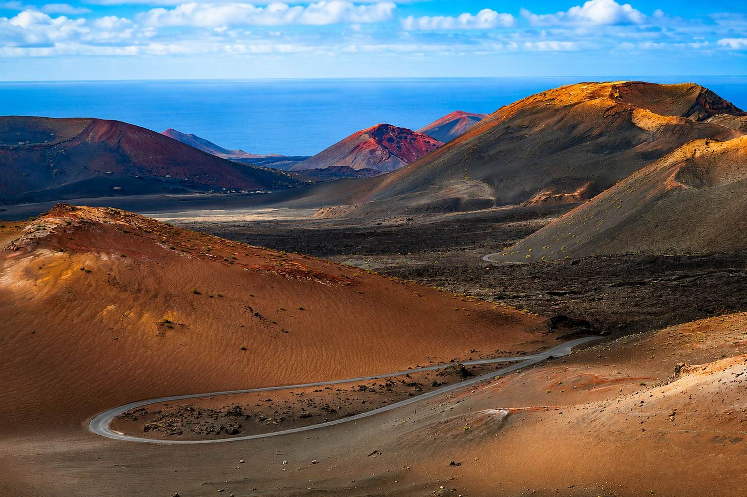 Un camí sinuós travessa un paisatge àrid, amb muntanyes llunyanes i un cel serè.