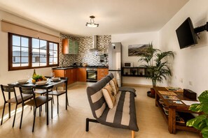 A modern kitchen with a dining area, a sofa, and a TV mounted on the wall. - Casa Carla Terraza BBQ y Jard n Volc Nico (Tinajo)