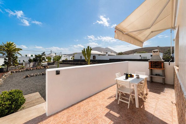 A terrace with a table and chairs, a barbecue grill, and a view of buildings and mountains. - Casa Carla Terraza BBQ y Jard n Volc Nico (Tinajo)