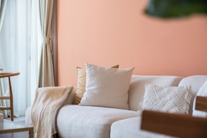 Ein Sofa mit vielen Kissen und einer Decke, vor einer pfirsichfarbenen Wand platziert.