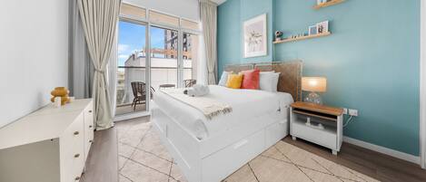 A modern bedroom with a large bed, a nightstand, a desk, and a view of the outside.