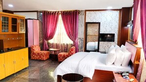 A hotel room with a bed, a desk, a chair, a small table, a cabinet, and a television. - Galaxy La Palm Royal Resort Abakaliki  (Abakaliki)