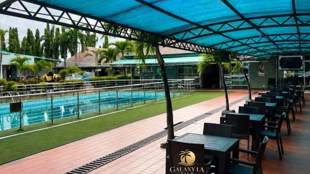 A covered outdoor area with a pool, chairs, and a sign for Galaxy La Palm. - Galaxy La Palm Royal Resort Abakaliki  (Abakaliki)