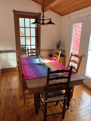 A dining area with a wooden table, chairs, a colorful tablecloth, and a hanging light fixture.