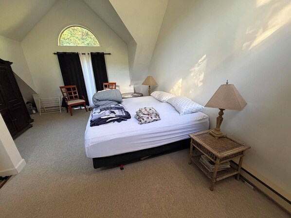 A bedroom with a large bed, a window, a chair, a lamp, and a small table.