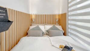 Un dormitorio con cama, almohadas, una mesita de noche, un cartel en la pared y una ventana con persianas.