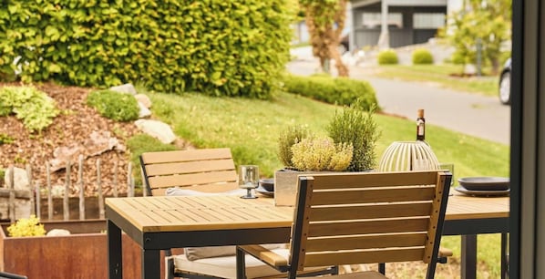 An outdoor dining area with a wooden table and chairs, a potted plant, and a bottle of wine.
