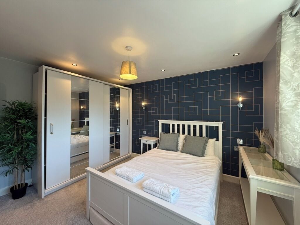 Ein Schlafzimmer mit einem Bett, Nachttischen, einem Kleiderschrank, einem Spiegel und einer Zimmerpflanze.