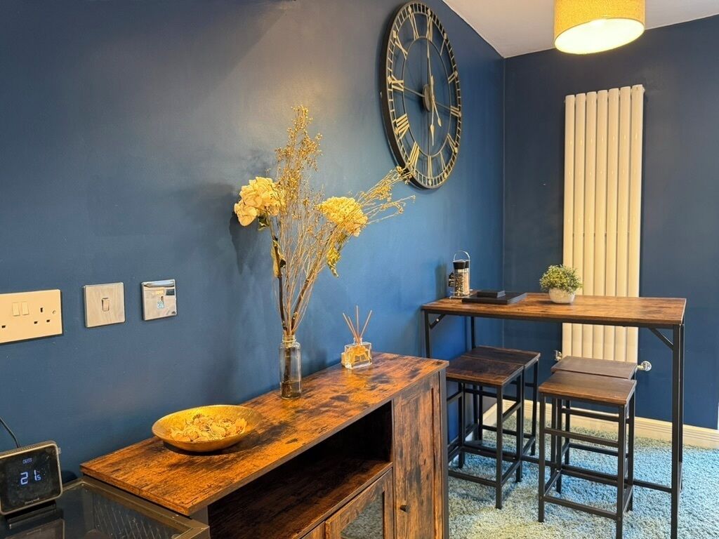 Une pièce avec un mur bleu, un banc en bois, une petite table, une horloge et un radiateur.