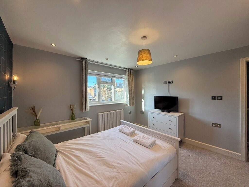A bedroom with a bed, a television, a window, and a radiator.